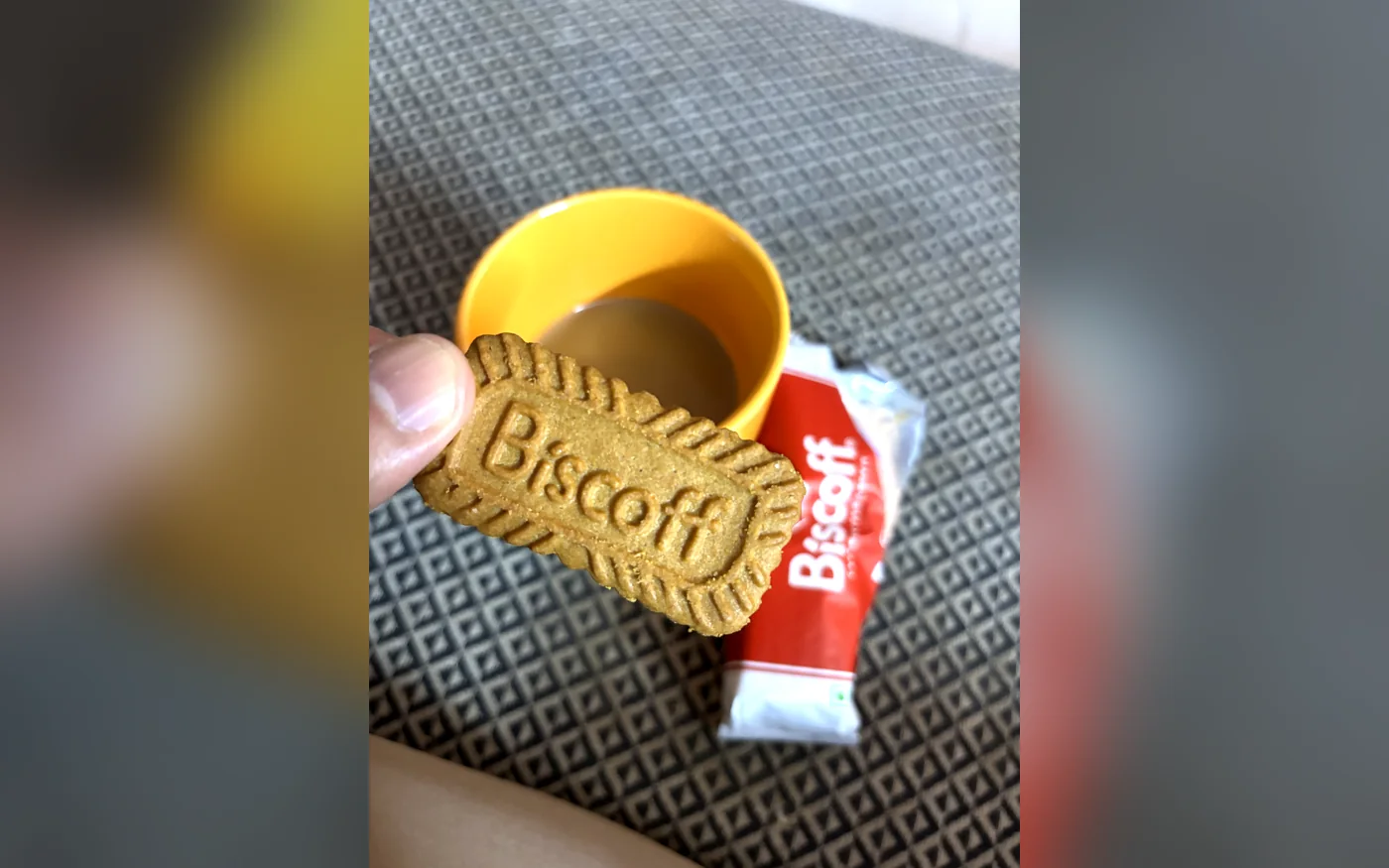 A Lotus Biscoff biscuit held beside a cup of chai on a desk