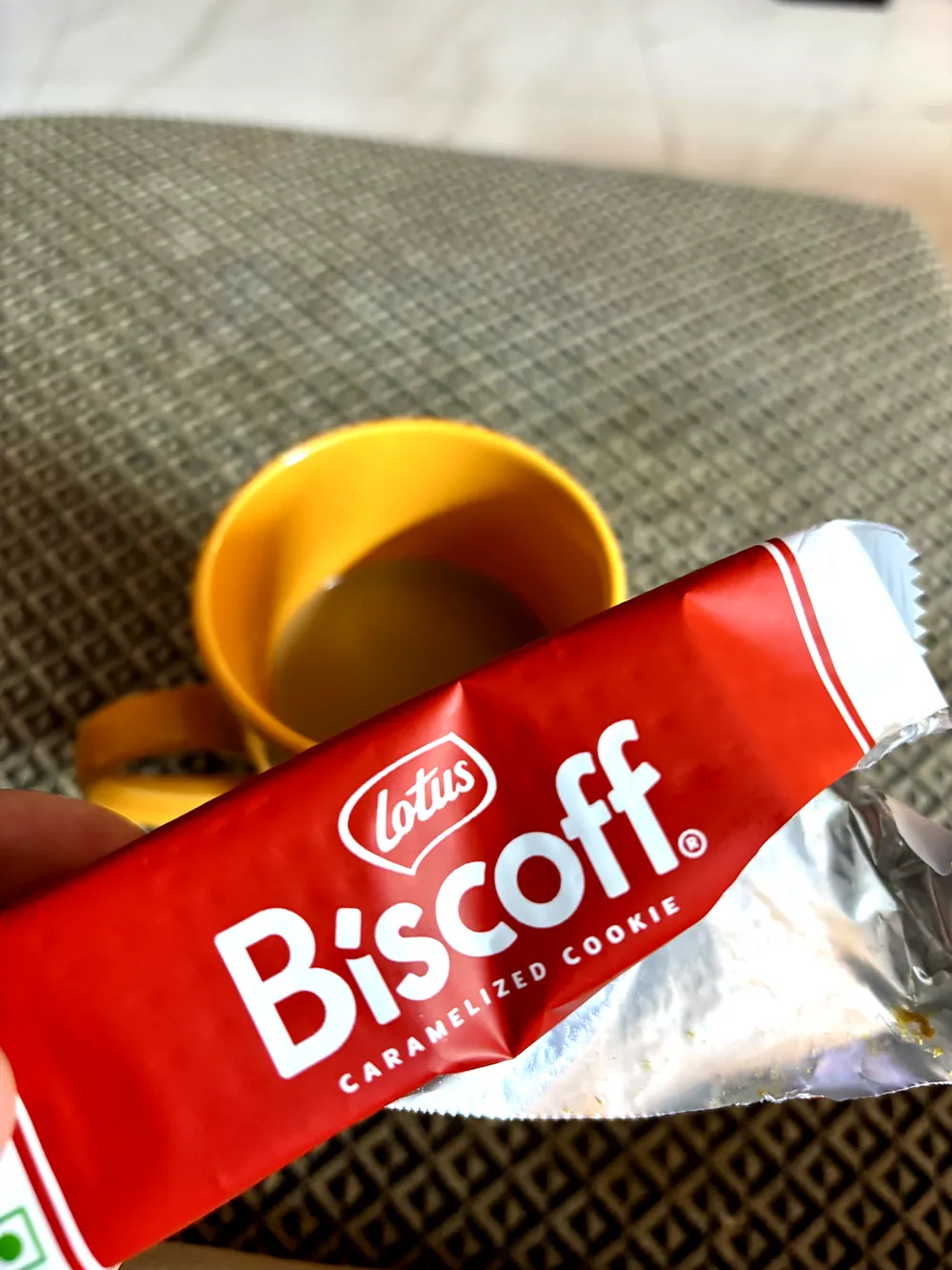 A Lotus Biscoff pack held over a yellow mug of chai