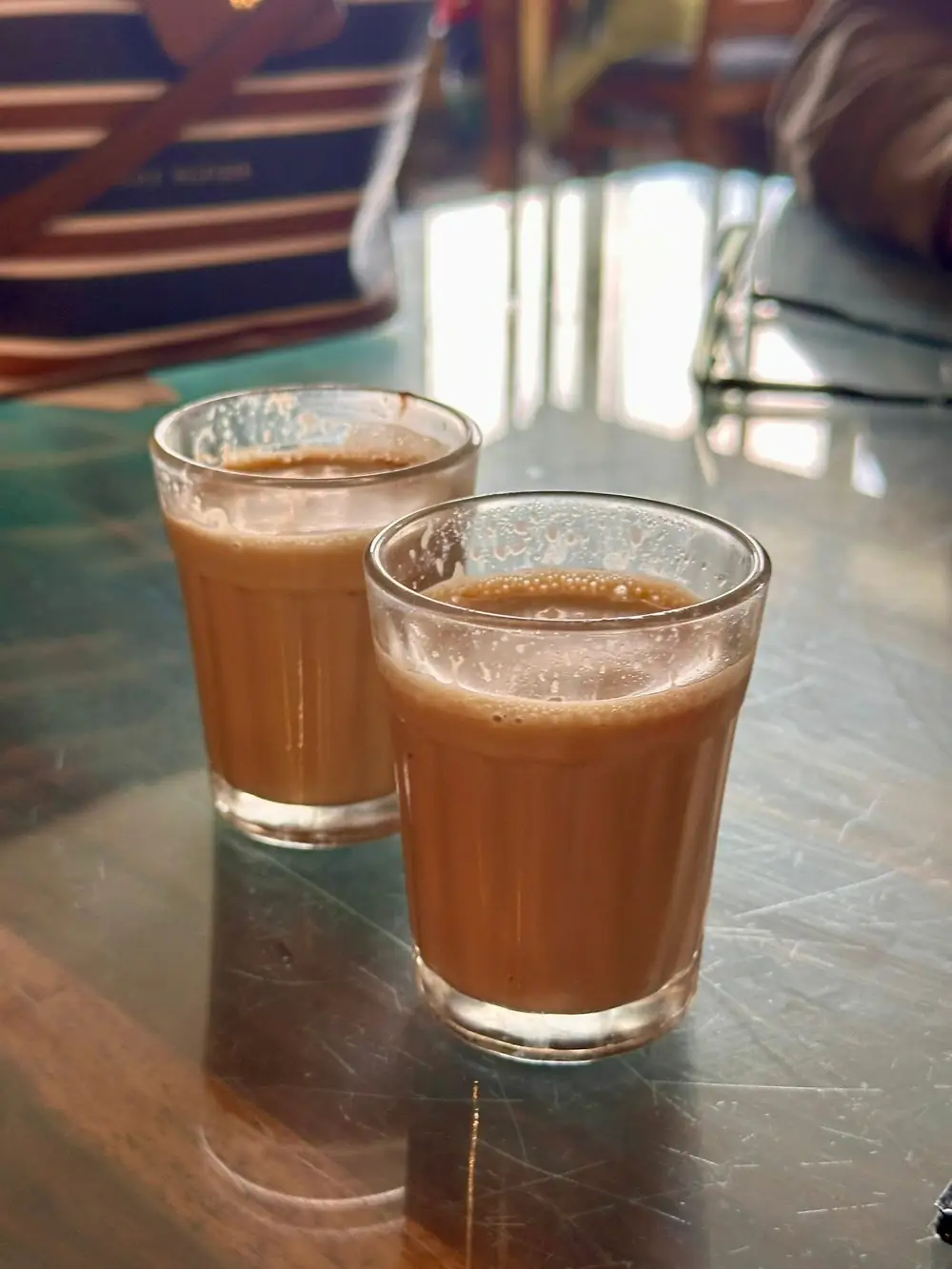 Two cutting glasses of masala chai on a steel dhaba table