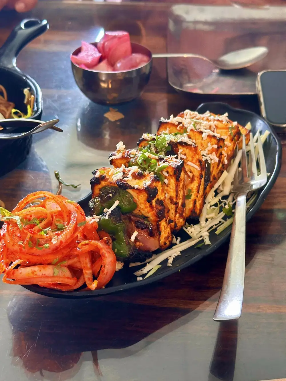 Paneer tikka with charred edges served on a black platter with masala onions