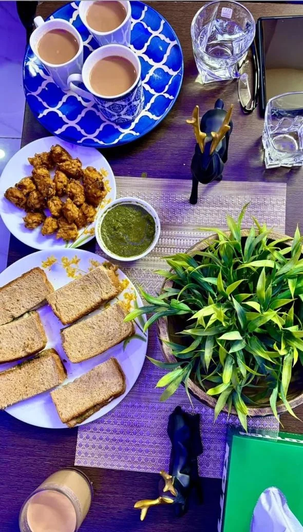 A table laid with cups of chai, a plate of pakode, green chutney and cucumber sandwiches