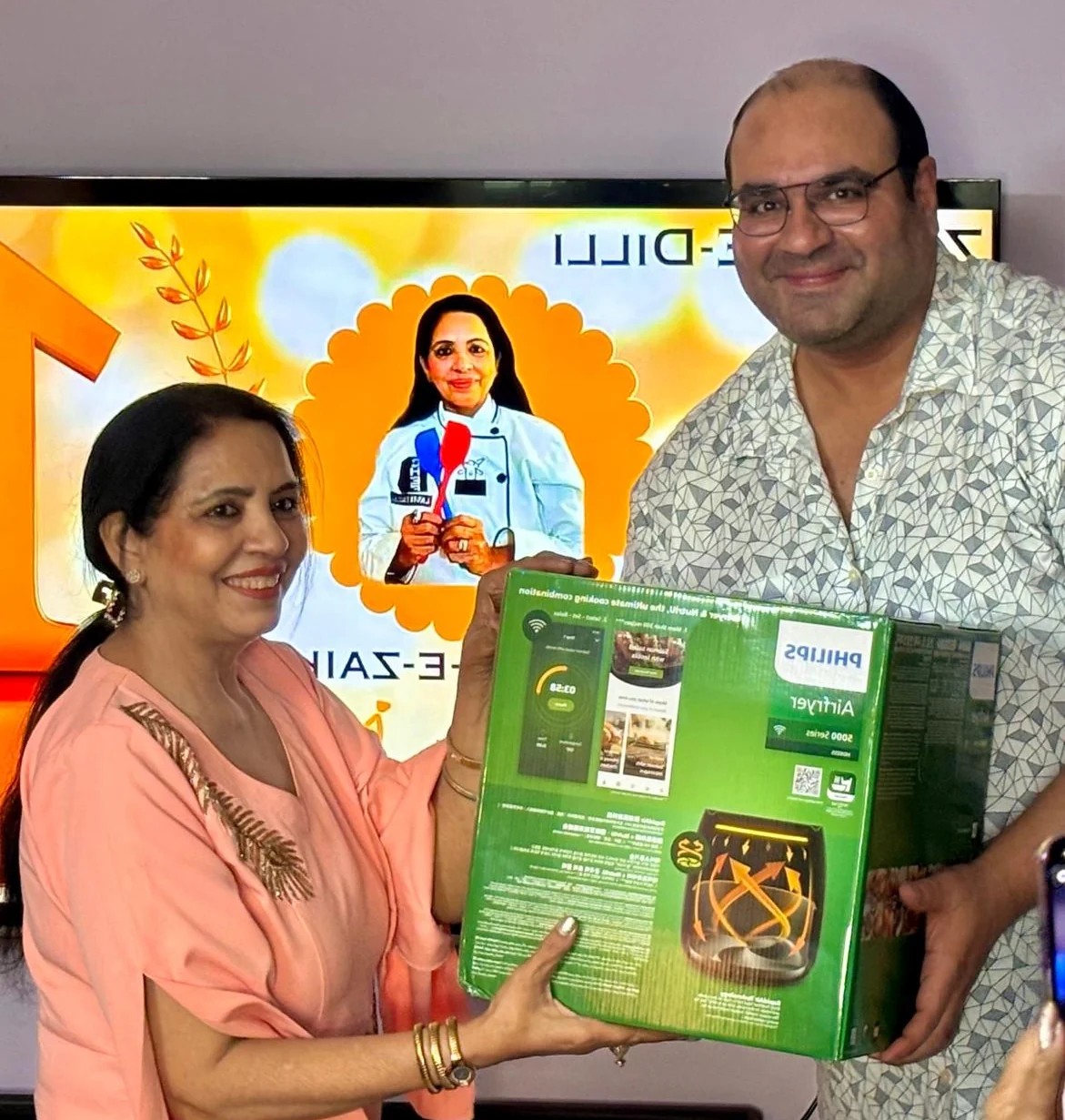 Laddi Dhingra receiving the Philips air fryer from Adit Kohli in front of the Mallika-e-Zaika announcement screen