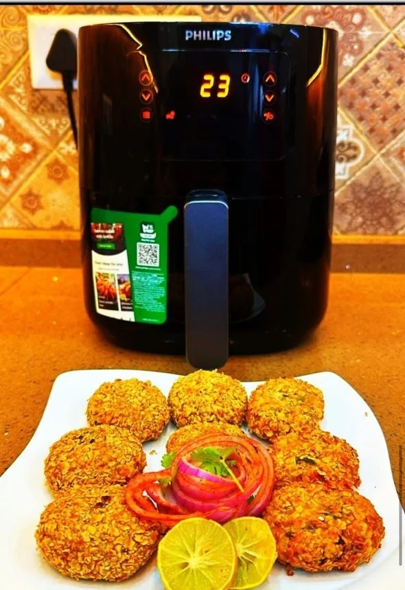 A plate of oats veg cutlets with sliced onion, tomato and lemon, in front of the air fryer