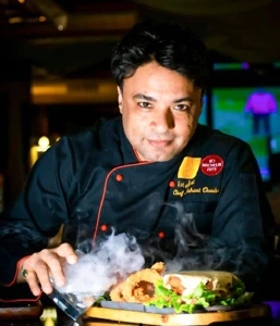 Chef Nishant Choubey plating a dish under smoke in a restaurant kitchen